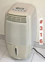 Front and side view of off-white Simplicity dehumidifier on tiled floor, showing vent grilles and water tank window.