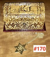 Full view of the carved jewelry box with an ornate design and gold-tone necklace with star pendant next to it.
