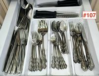 Drawer tray with various pieces of ornate stainless steel flatware and black handled steak knives organized in separate compartments.