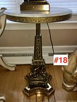 Full view of marble topped side table with ornate bronze or brass detailed base, showing its shape and height related to nearby furniture.