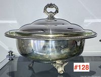 Silver plated serving dish with lid and glass liner, shown from angled side view on glass table.