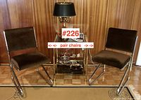 Two chrome cantilever chairs with brown upholstered seats and backs flanking a glass and brass bar cart on parquet floor.