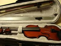 Violin laid inside open case with bow above it, showing the condition and arrangement.