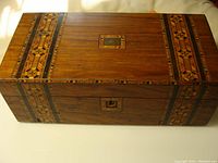 Full view of the antique wooden writing desk showing the rectangular form and marquetry pattern across the top and locking keyhole.