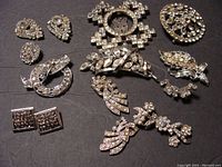 Overview of all 11 rhinestone brooches and clips laid flat on dark background showing design and size variety.