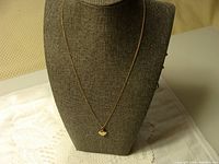 Full view of gold chain and heart locket displayed on a necklace bust stand.