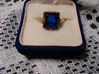 Front view of ring in display box showing square-cut blue rhinestone