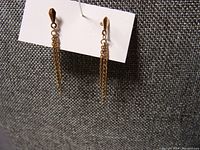 Pair of dainty 10K gold drop earrings hanging on a white card, showing the gold teardrop top and multiple fine chain dangles against a textured gray background