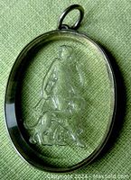 Close-up of the oval pendant showing the reversed carved glass depiction of Hunter Diana with dog inside the sterling silver frame on a fabric background.