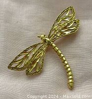 Overhead view of brooch on light fabric showing open-work wings and segmented body.