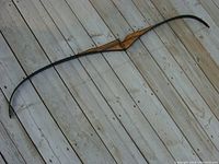 Full view of the vintage wooden bow laid on a wooden surface showing the entire 60 inch length and curved limbs.