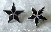 Close-up of two star-shaped sterling silver earrings with black inlay showing condition and design details.
