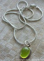 Close-up of pendant on chain, showing oval green prehnite stone with bezel setting and part of chain.