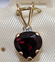 Close-up image of heart-shaped garnet pendant in 10K yellow gold, showing prong settings and small clear accent stone.