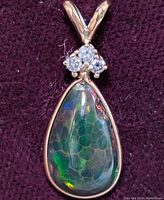 Close-up photo of the 14K gold pendant with colorful teardrop opal and three small diamonds on a dark purple background.