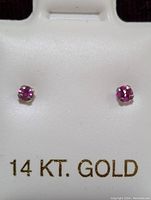 Pair of 14K white gold stud earrings with ruby gemstones in prong settings. Displayed on a white holder marked '14 KT. GOLD'.