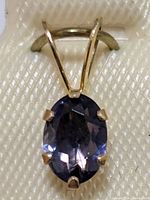 Close-up front view of the oval faceted tanzanite stone set in a 14K yellow gold prong setting pendant on a white display card