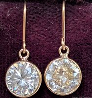 Close-up front view of round moissanite stones set in 10K gold earrings on purple velvet background.