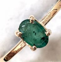 Close-up of oval natural emerald set in 10K gold ring showing prong setting and gemstone inclusions