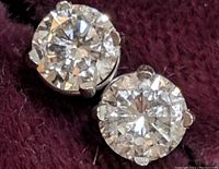 Close-up of two round brilliant cut diamonds in four-prong white gold settings on dark purple background