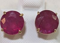 Front view of two round faceted ruby studs set in 14K yellow gold four-prong settings on white display