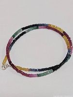 Full view of the multi-colored mixed sapphire and emerald faceted bead necklace coiled flat showing the vibrant colors and pattern.