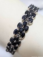 Close-up photo of sterling silver bracelet with double rows of oval faceted blue sapphires on white display.