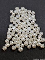 Multiple loose fresh water pearls of various sizes and shapes arranged on a black surface.