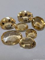 Seven oval faceted citrine gemstones laid out on a white surface showing pale yellow to golden hues.