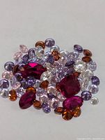 Pile of multi-colored cubic zirconia stones in various shapes and sizes, including reds, purples, clear, amber, and light pinks.