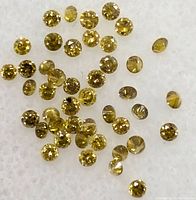Close up view of multiple small, loose yellow round cut diamonds spread on a white surface.