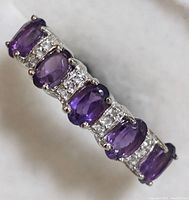 Close-up angled view of sterling silver ring with five oval amethyst stones and white topaz accents.
