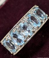 Close-up front view of sterling silver ring with five oval blue topaz stones, showing facets and prong settings