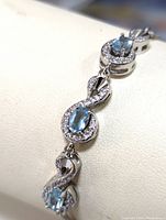 Close-up of bracelet showing oval blue topaz stone set within an infinity-shaped frame with cubic zirconia stones.