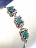 Close-up showing three oval emerald stones each surrounded by cubic zirconia, set in sterling silver.