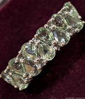 Close-up photo of sterling silver ring featuring multiple green sapphire gemstones arranged side by side in pear shapes, showing detail of prong settings and stone clarity.