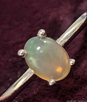 Close-up photo of sterling silver ring with oval opal cabochon stone, showing iridescent green and orange colors.