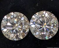 Close-up photo of two round-cut moissanite stones on black background showing brilliance and faceting.