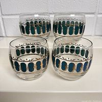 Four round lowball glasses with teal oval and gold trim designs shown from the front view.