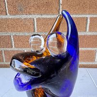 Front view of the blue and amber colored glass dancing couple figurine showing detail of intertwined forms and clear glass heads against a brick background.