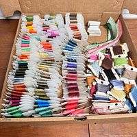 Box of over 100 embroidery thread skeins wrapped on white holders arranged by color.