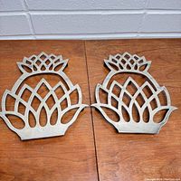 Two metal pineapple shaped trivets side by side on wooden surface