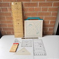 Photo showing all items in lot including large acrylic ruler, two Quilter's Cut 'n Press I pressing tools, small rulers, and transfer paper.