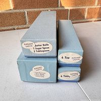 Stacked original blue boxes labeled with Elegant Lady pattern and contents including butter knife, sugar spoon, tablespoons, cold meat fork, pastry server, icing lifter, and teas for teaspoons.