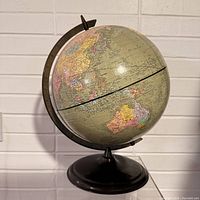 Side view of vintage world globe showing Asia and Australia regions mounted on black metal base with partially visible meridian axis.