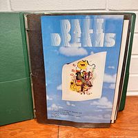 Front view of an open page in the green binder showing a Dali Dreams art flyer with surrealistic illustration and text.