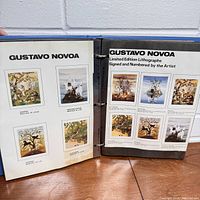 Open blue binder showing two pages featuring limited edition lithographs signed and numbered by artist Gustavo Novoa, with small images of various paintings and their details.