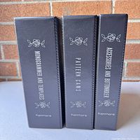 Three gray hardcover accessory cases with white floral decoration and text indicating contents as Monogrammer and Templates, Pattern Cams, and Accessories and Buttonholer by Kenmore.