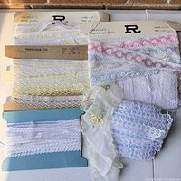 Vintage lace trims in white, yellow, and pink hues on original cards alongside loose embroidered sheer lace and knitted lace pieces.