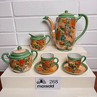 Full tea set including teapot, creamer, sugar bowl, two cups, and two saucers displayed on a tiered white stand showing floral and bird decoration in lustreware marked Japan.